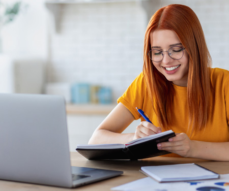 Teen girl writing in journal by a laptop